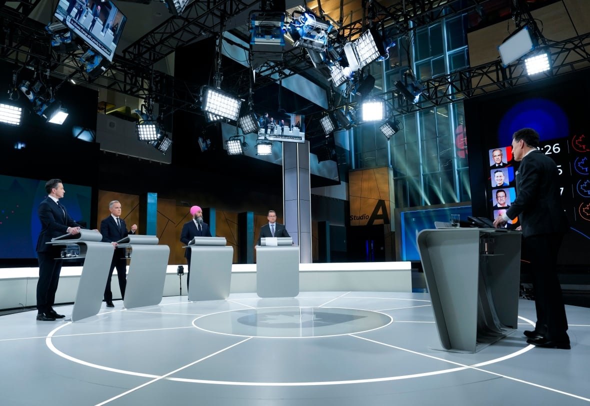 Four men stand at lecterns on a stage.