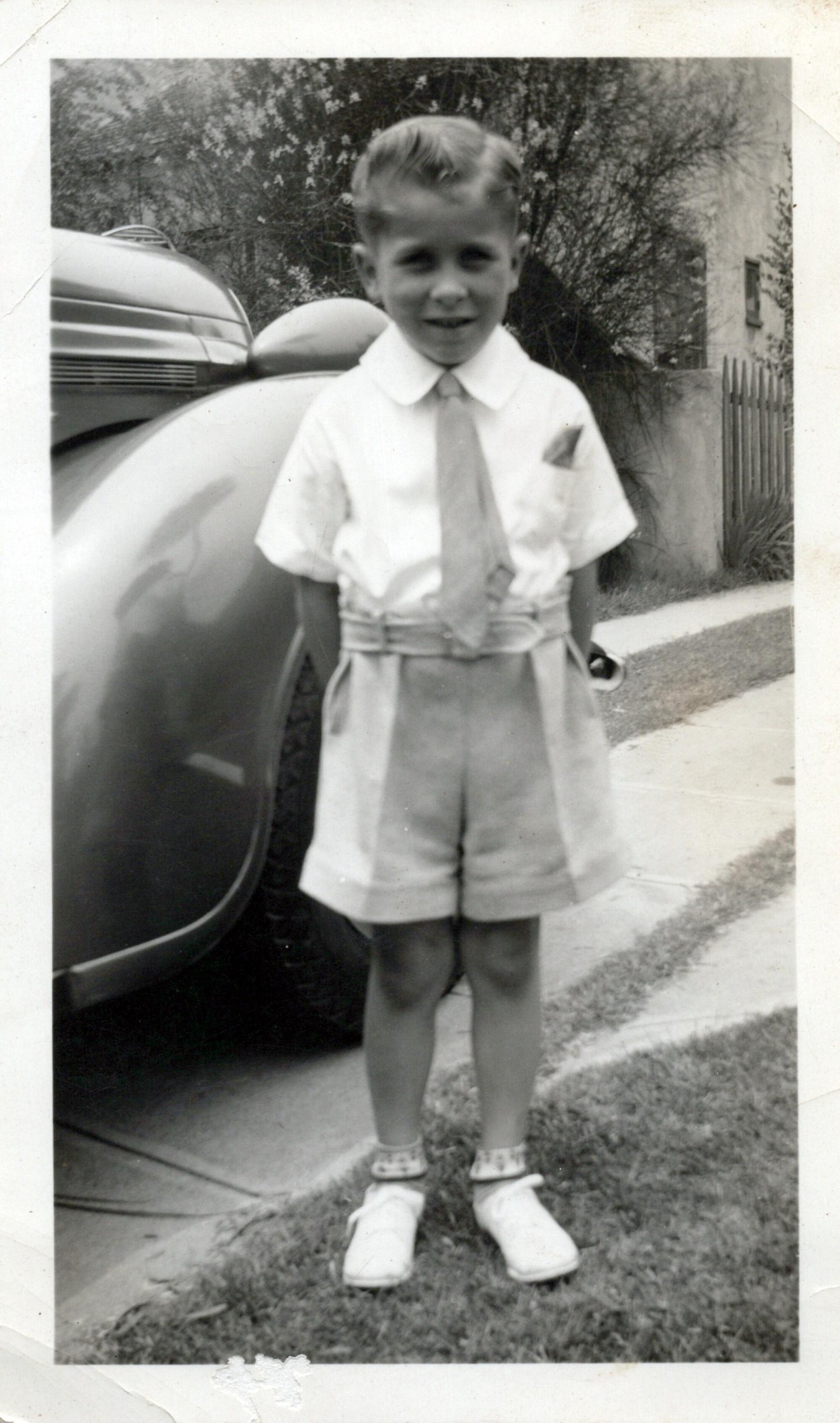 A young boy in a collared shirt with a tie and shorts. 
