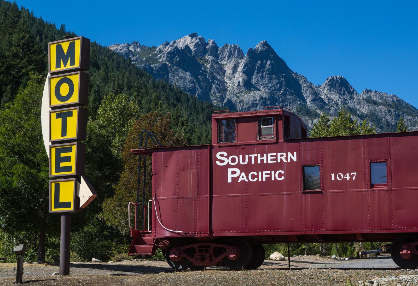Castle Crags, a jagged geological rock near Dunsmuir, rises behind a red Southern Pacific railcar.