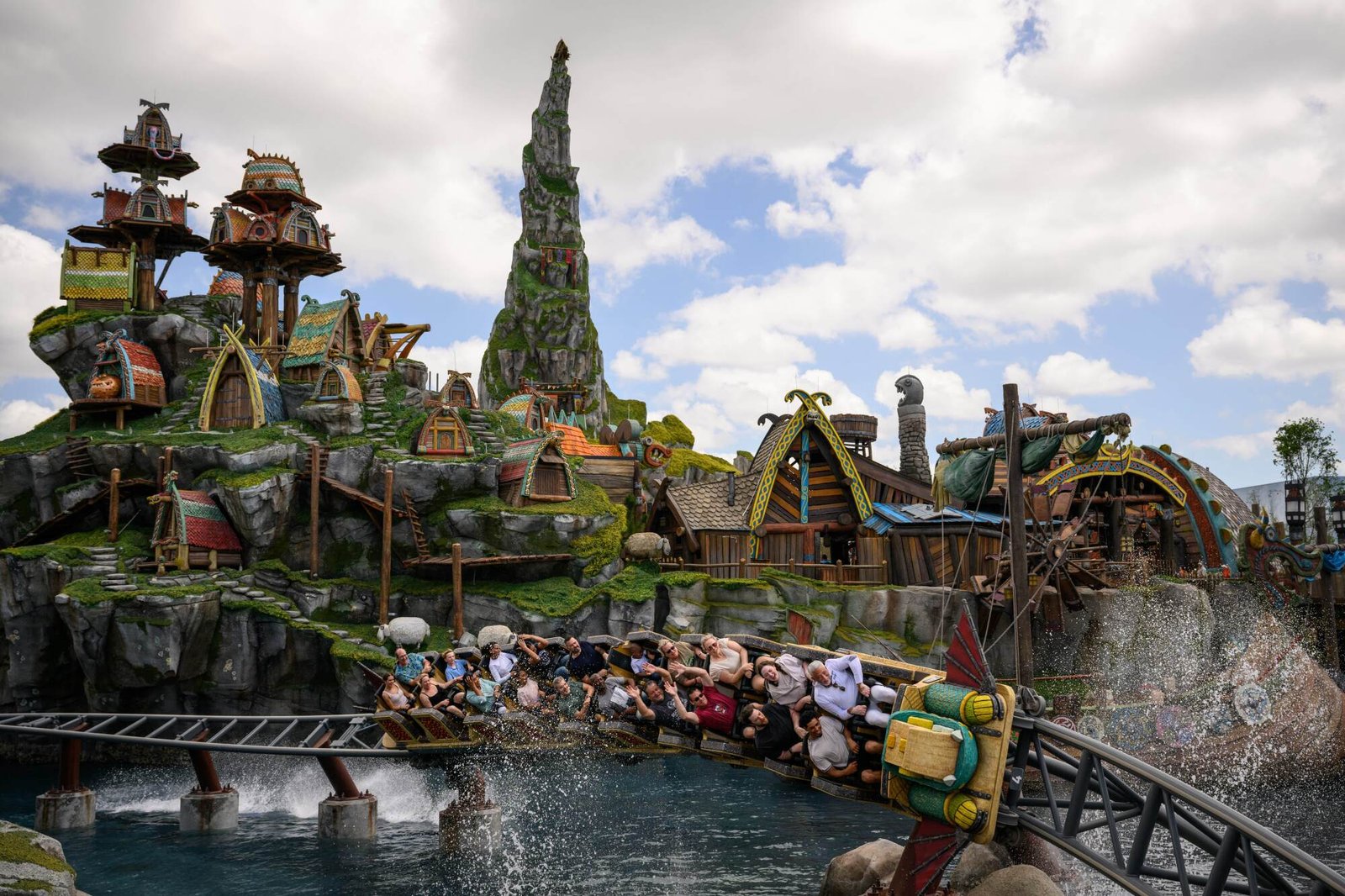 A family coaster careens over water and under built mountains