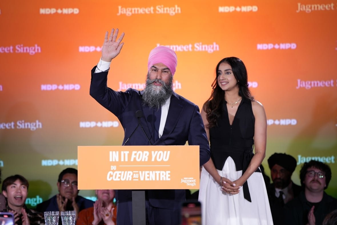 A man waves standing beside a woman at a podium.