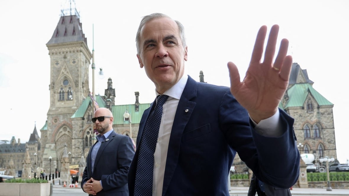 A man wearing a suit and tie waves in front of a building.
