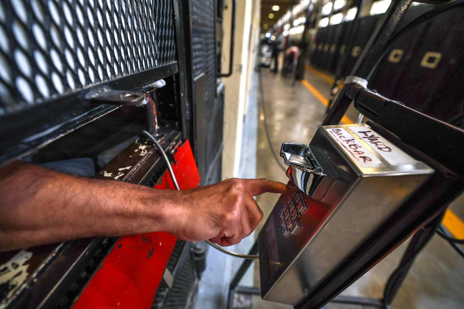 A hand reaches through a prison cell opening to dial a phone stationed just outside.