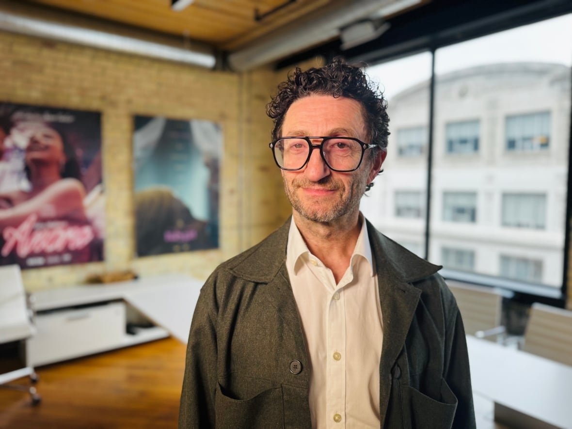 A man wearing glasses stands in a modern office building.