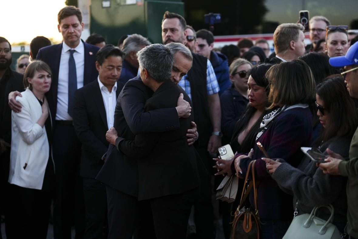 A man and woman embrace in the middle of a crowd of mourners.