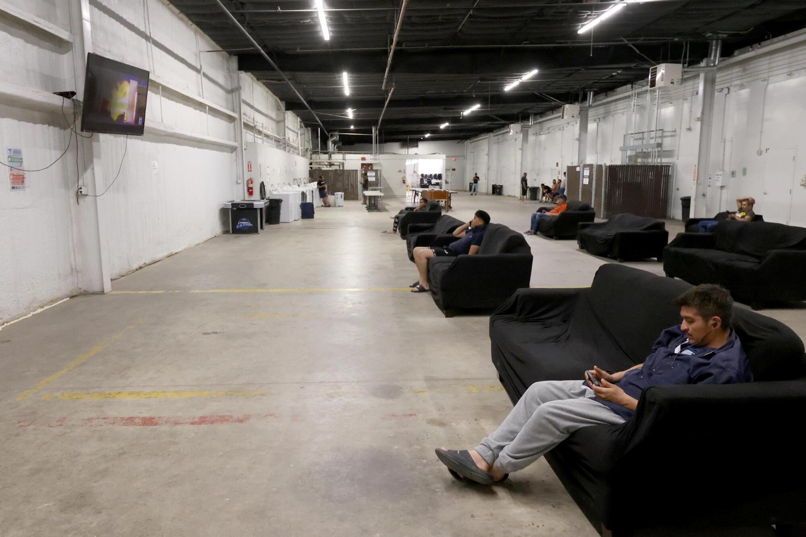 Migrants relax on black couches in a large community room at an H-2A guest housing site.