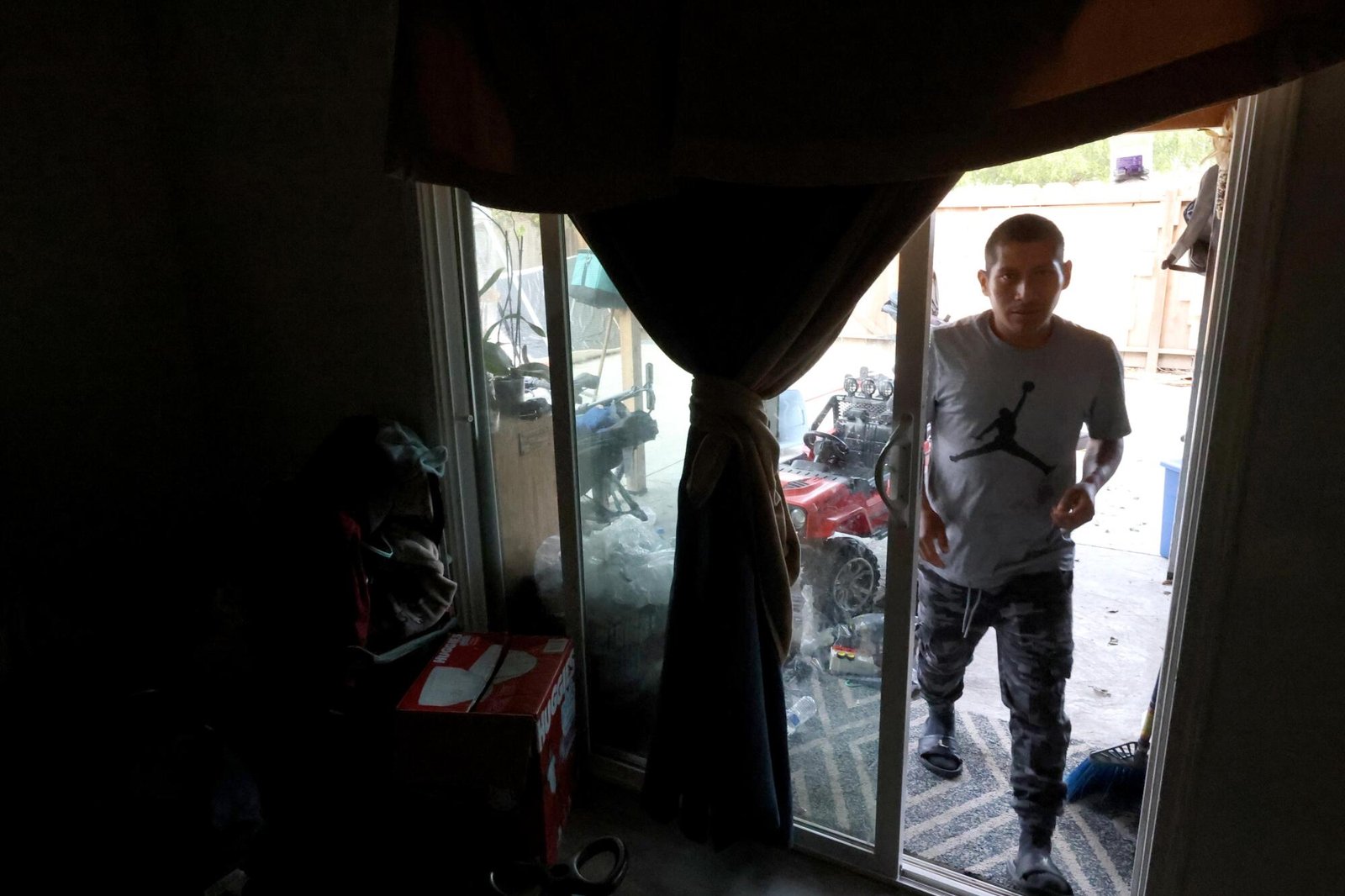 A man enters a darkened home through a sliding glass door.