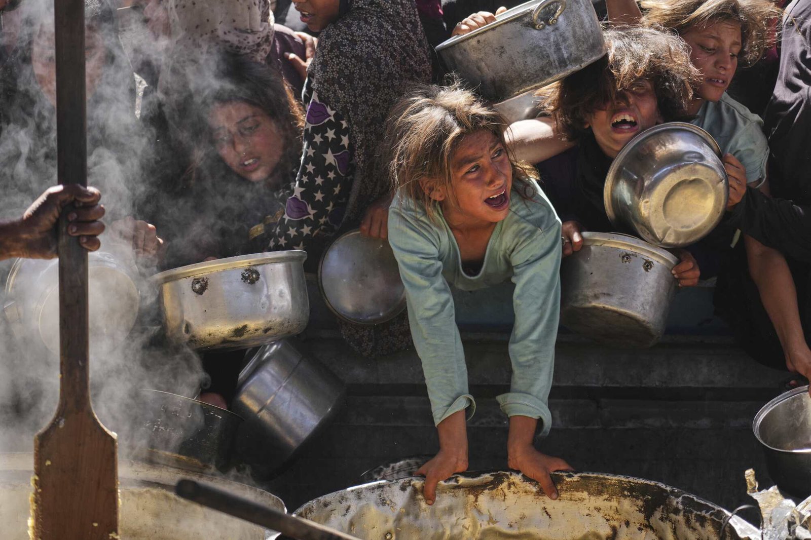 Palestinians carrying bowls struggle to get donated food at a community kitchen