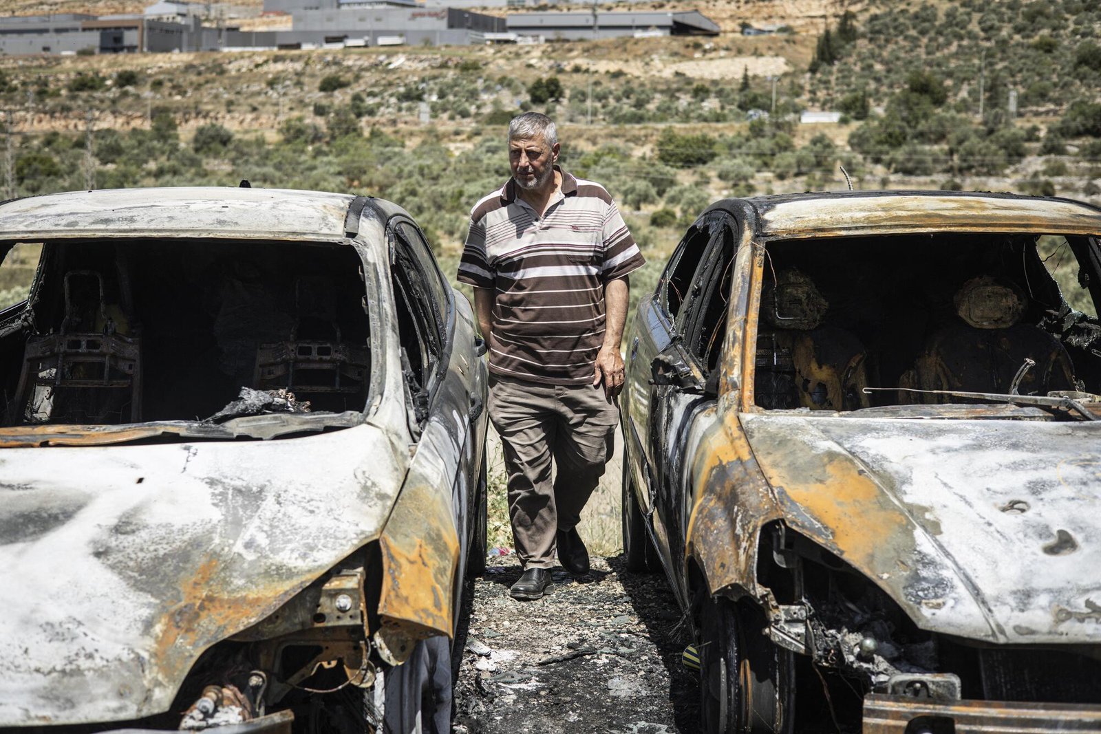 A man looks at burned vehicles