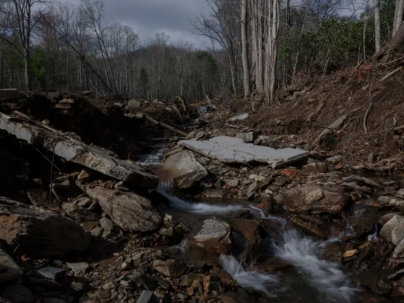 A creek rushes below chunks of a home’s foundation in the middle of a forest.
