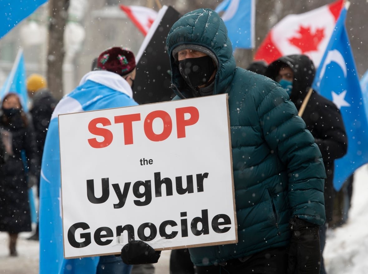 A man in heavy winter clothing holds a placard reading 'Stop the Uyghur genocide'