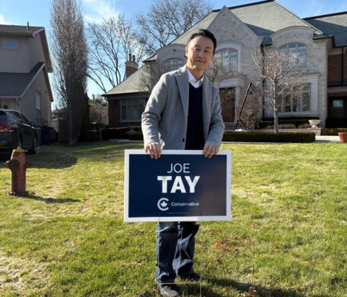 A man poses on the front lawn of a house with an election sign reading 'Joe Tay'