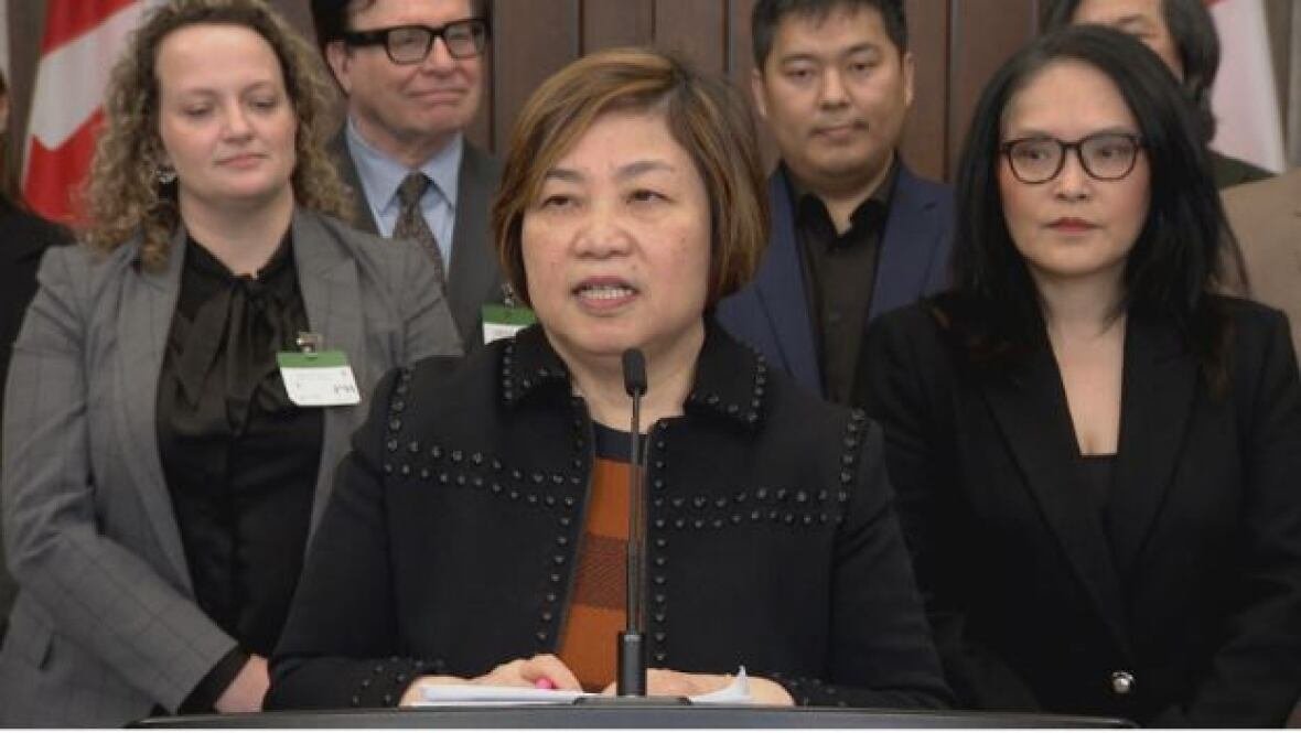 A woman speaks at a microphone, flanked by other women and men. 