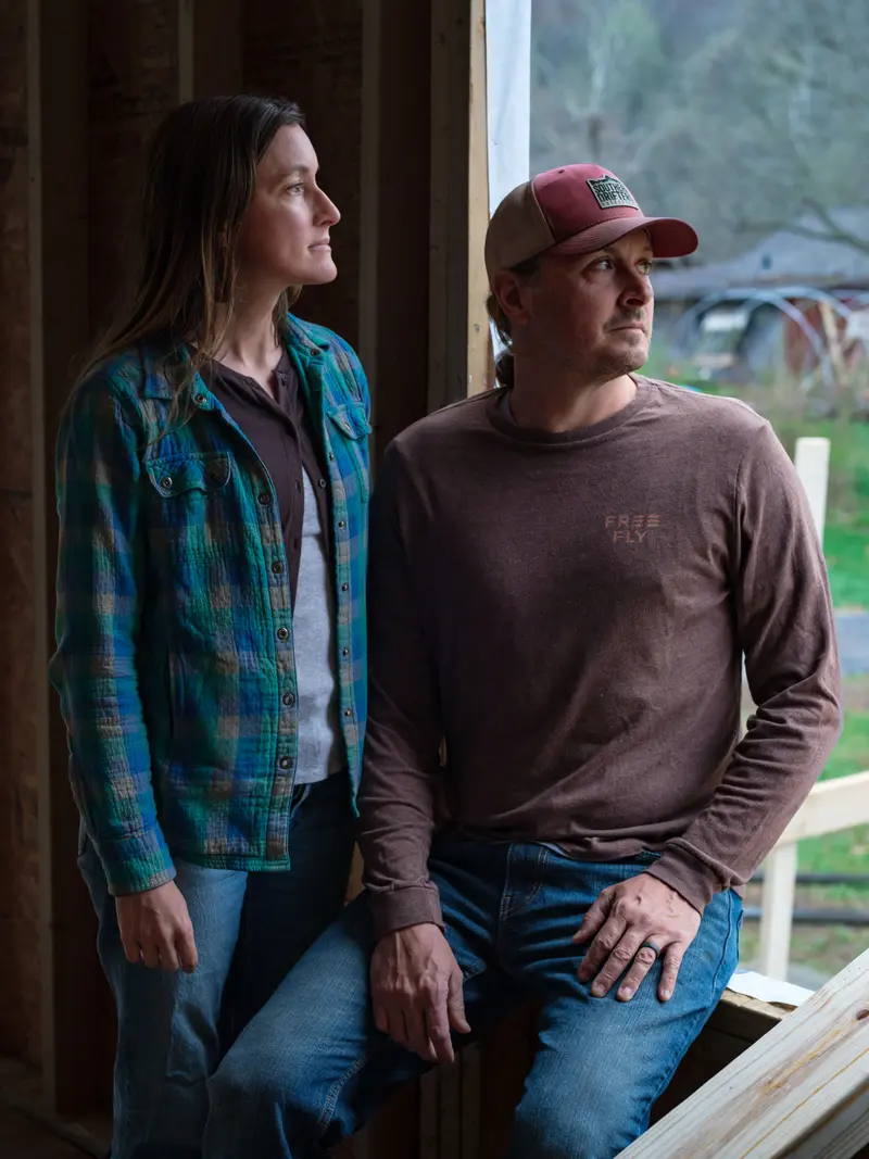 A woman and a man look out from a dark building onto a landscape.