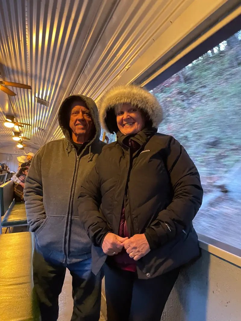 A man and woman stand smiling next to a window.