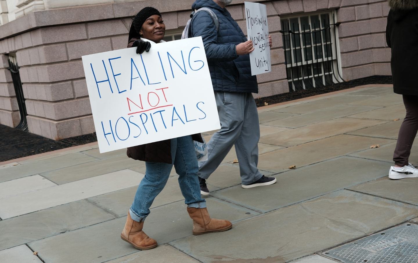 A woman holds a sign protesting NYC Mayor Eric Adams’s policy on mental health
