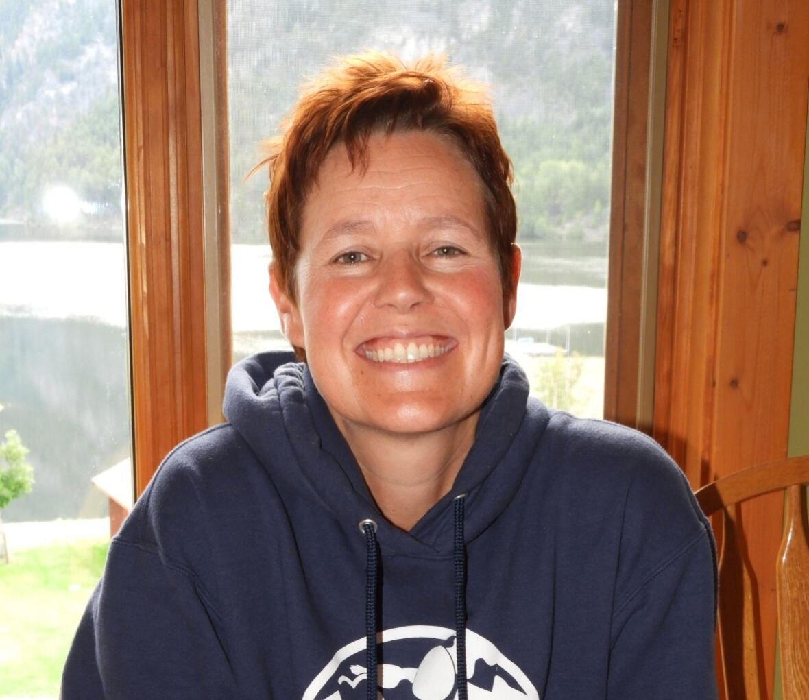A woman with short red hair smiles for a photo, wearing a navy blue hoodie.