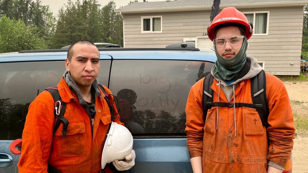Two men in firefighting gear pose in front of a minivan with the words "big betty" traced into the dust on one of its windows.