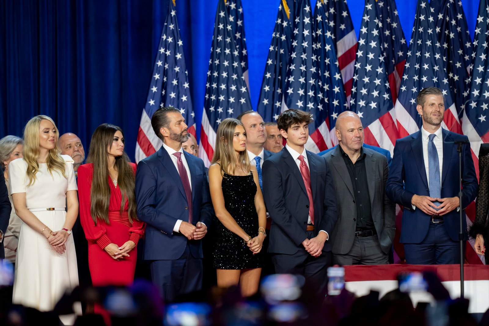 From left, Susie Wiles, Tiffany Trump, Tony Fabrizio, Kimberly Guilfoyle, Donald Trump Jr., Walt Nauta (hidden two people), Kai Madison Trump, Dan Scavino, Corey Lewandowski, Donald Trump III, Dana White, Chris LaCivita and Eric Trump, listen as Republican presidential nominee former President Donald Trump speaks at an election night watch party Wednesday, Nov. 6, 2024, in West Palm Beach, Fla.