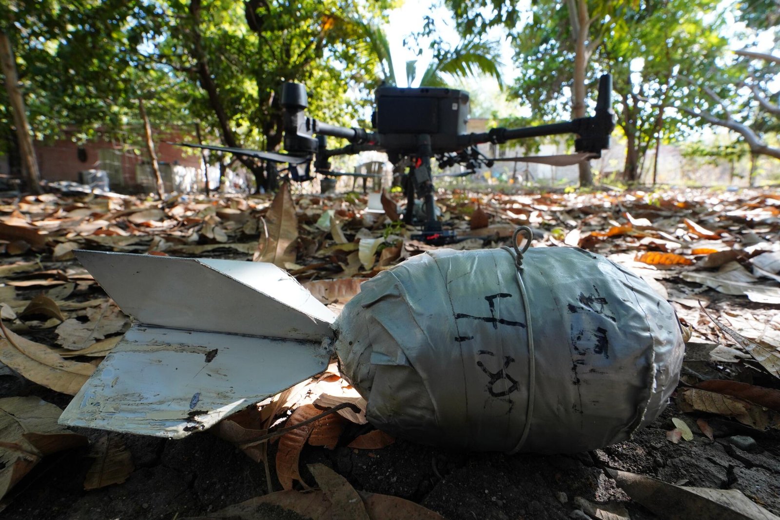 A close-up of an improvised bomb and a drone at rest among leaves on the ground