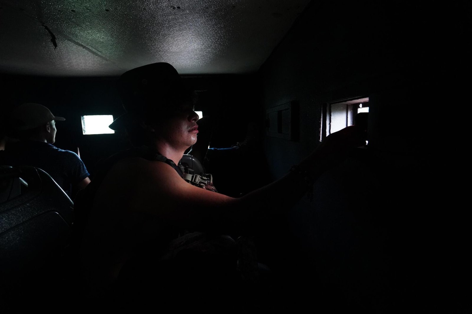 A cartel commander in the dim interior of a makeshift armored vehicle