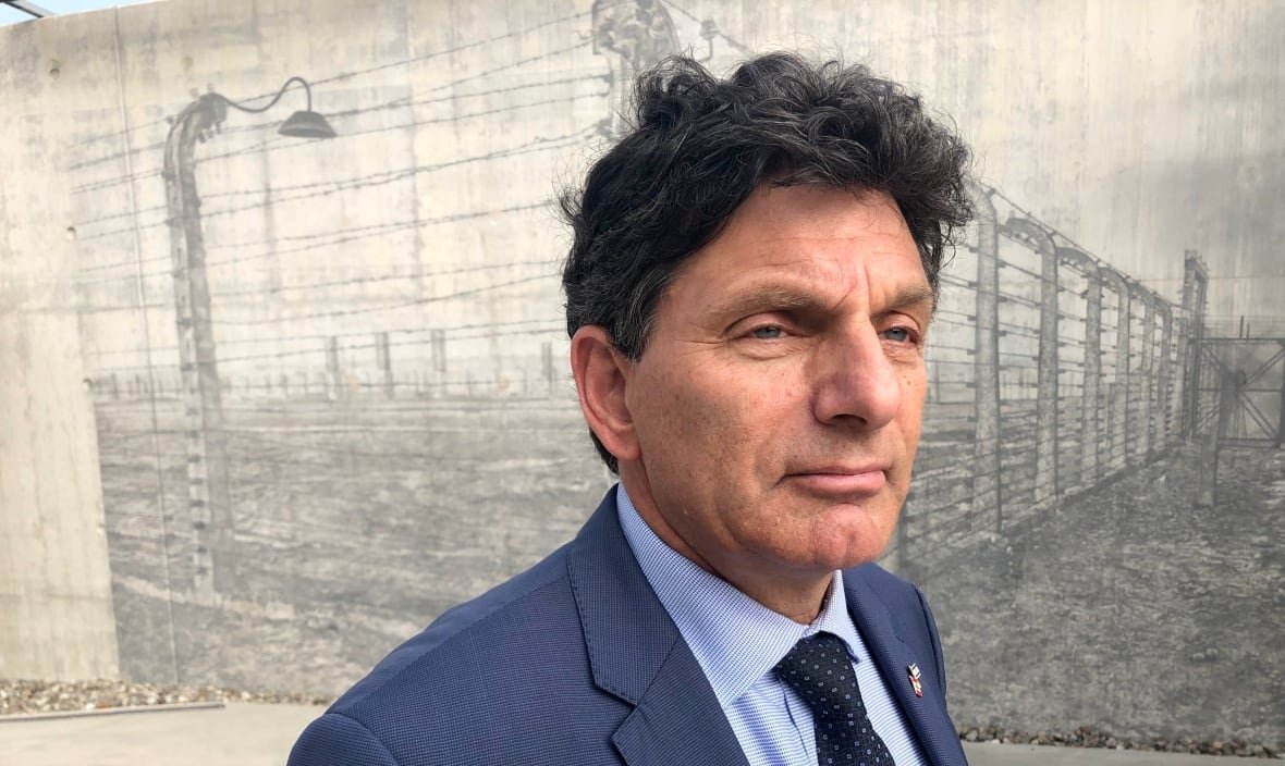 A man in a suit stands in front of an etching of a concentration camp on the concrete of the National Holocaust Memorial.