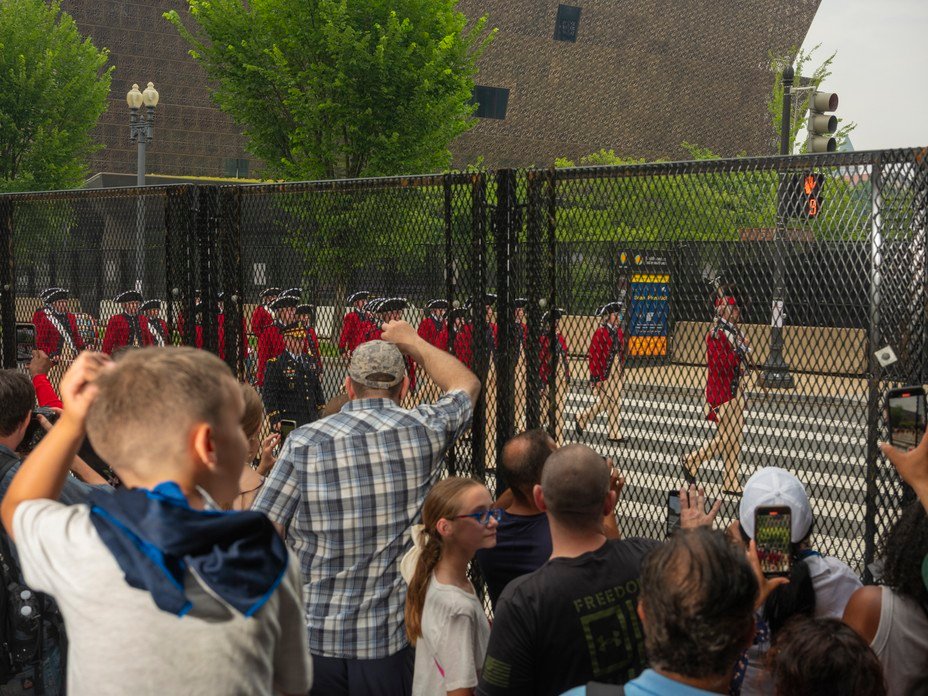 Picture of crowds watching the Old Guard Fife and Drum Corps from behind barricades near the National Museum of African American History.