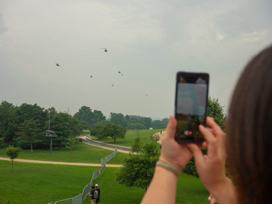 Picture of an observer photographing military helicopters flying in formation through cloudy skies. 