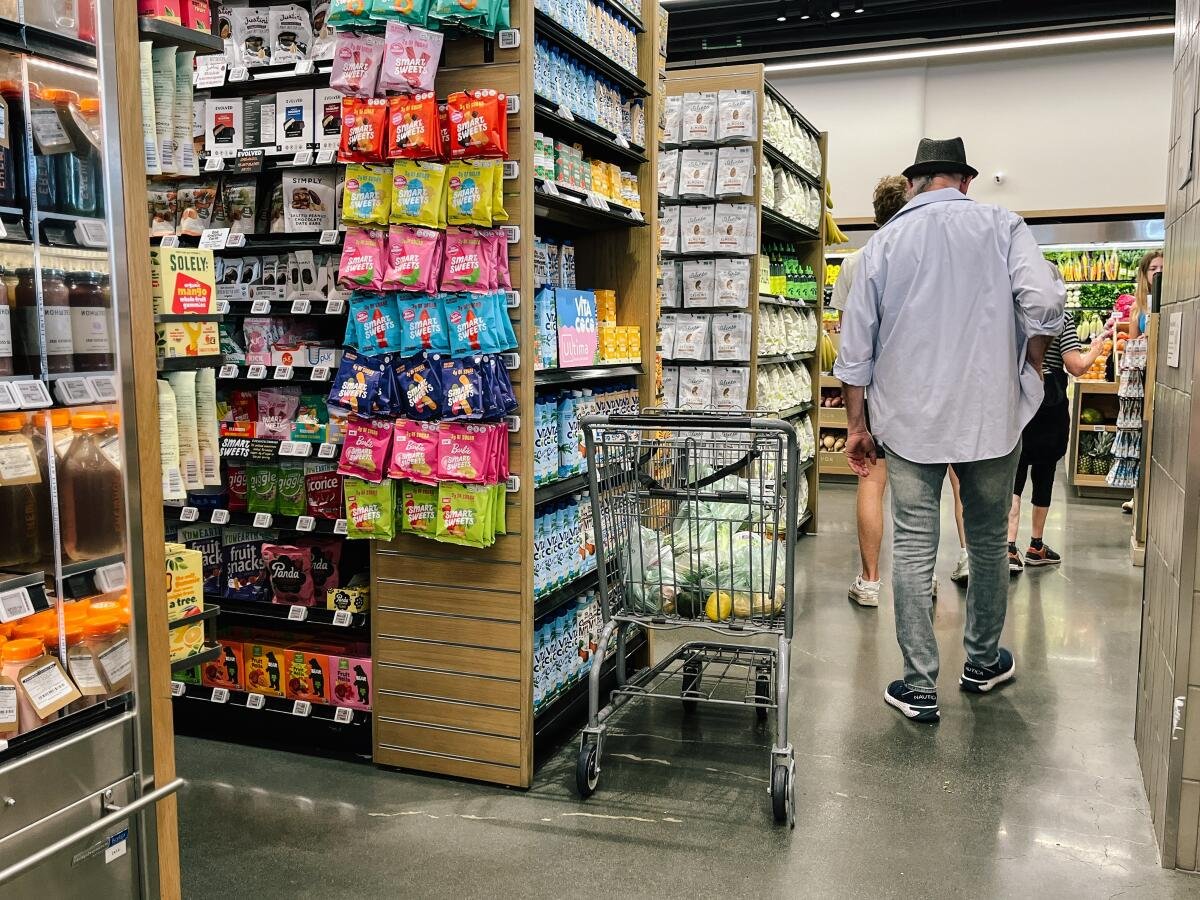 A man walks by a shopping cart in a grocery store aisle.