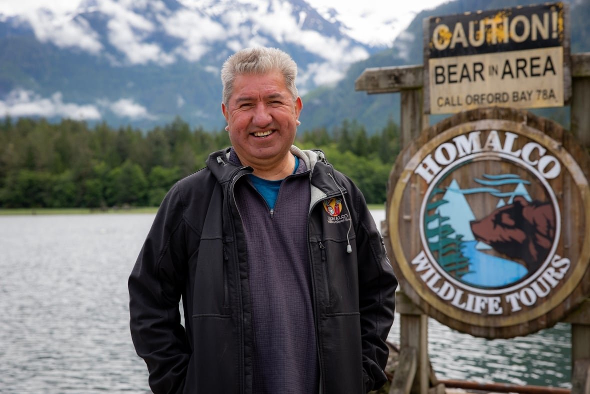 A smiling Indigenous man with white hair stands on a dock.