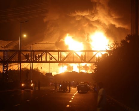 People watch from a bridge as flames from an Israeli attack rise from Sharan Oil depot at the weekend