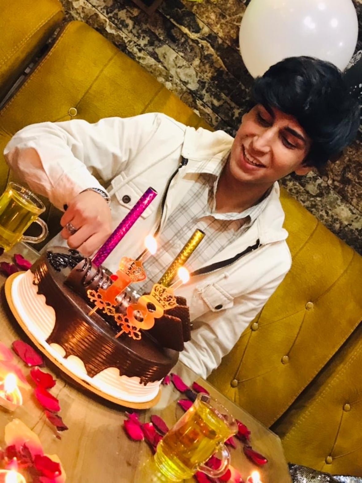 A young man sits in front of a birthday cake with candles and the number 18 on it.