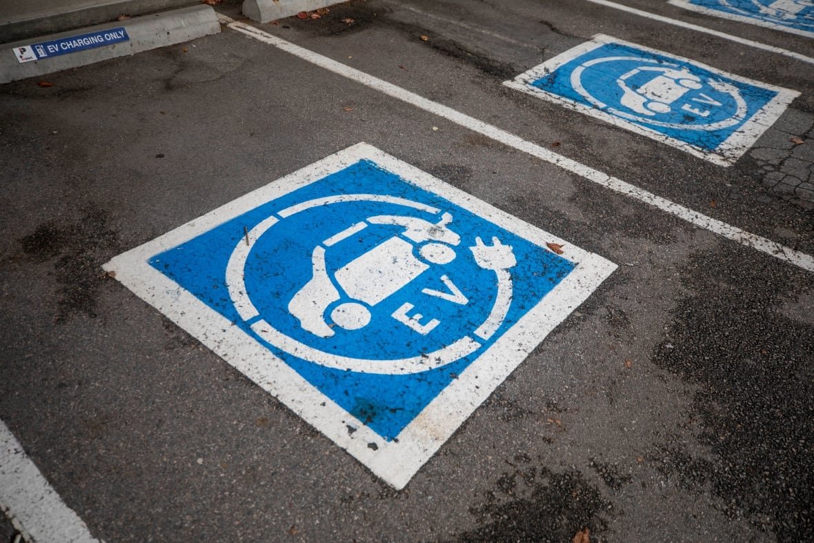 Blue and white EV symbols are painted on asphalt to mark parking stalls.