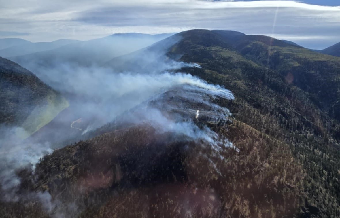 An aerial shot of smoke rising from mountainous hills. 