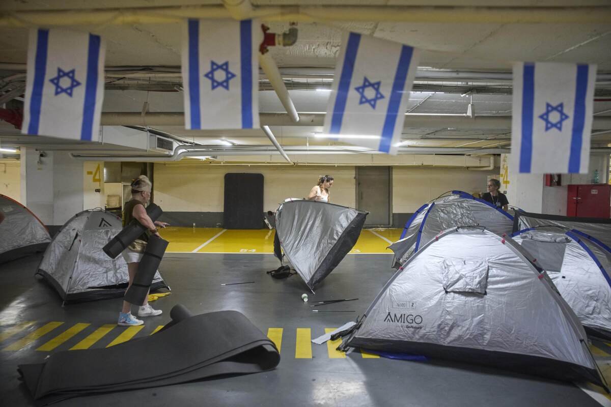 People fold silver-colored tents under blue and white flags with stars