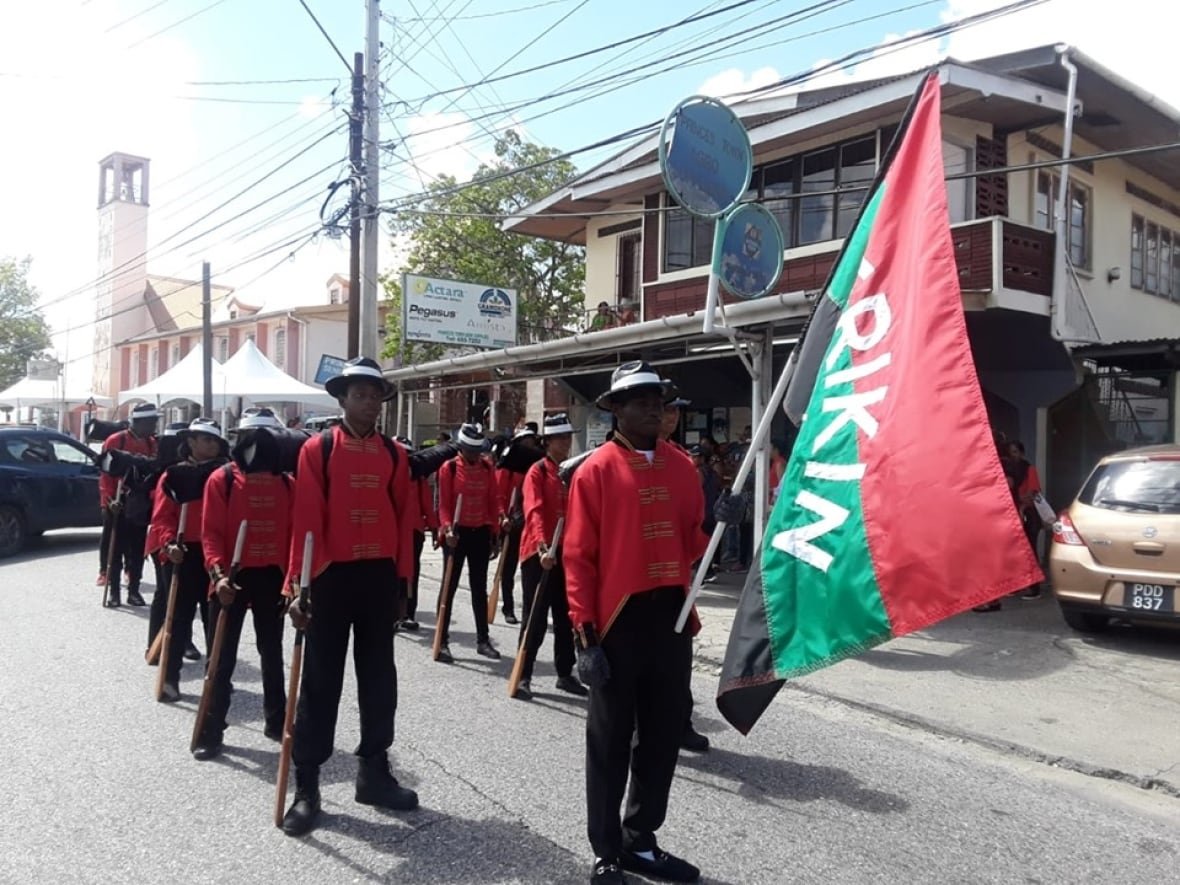 Merikin descendants take place in a parade in military uniform led by a flag bearer.