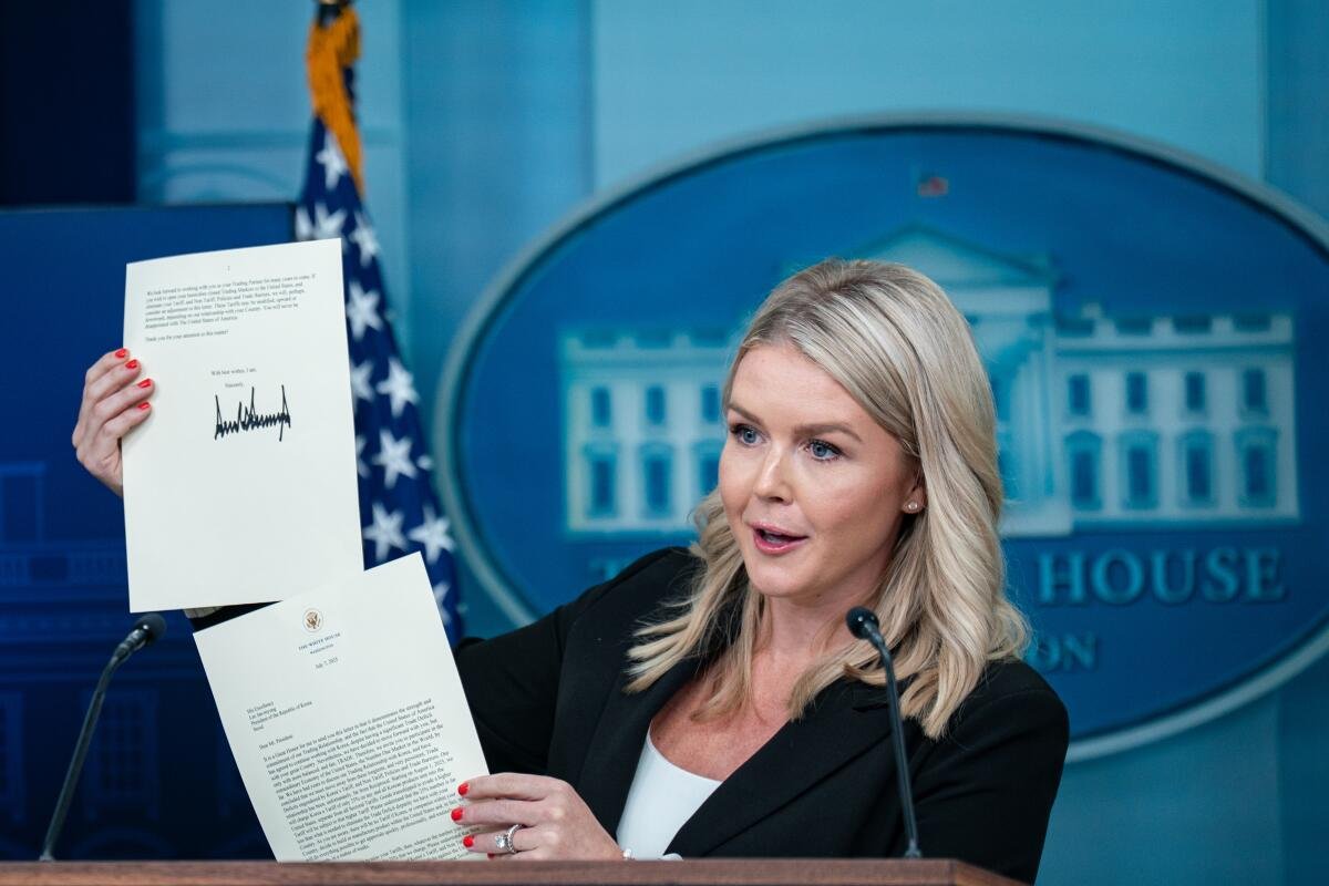 Press Secretary Karoline Leavitt holds up two pages of a letter while speaking into a microphone at a White House conference