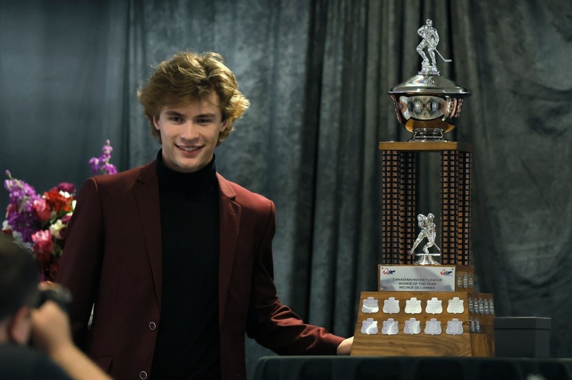 A young man in a sport coat poses with a trophy.
