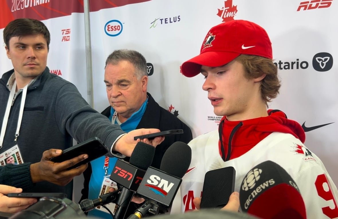 A young hockey player in a media scrum. There are two other men to his left.