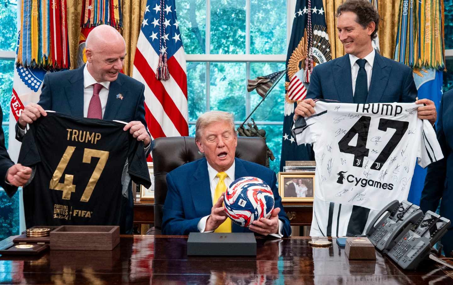 President Donald Trump flanked by Ferrari chair John Elkann (R) and FIFA president Gianni Infantino, holds a ball as he makes remarks in the Oval Office of the White House during a visit by members of Italian soccer club Juventus in Washington, DC, on June 18, 2025.