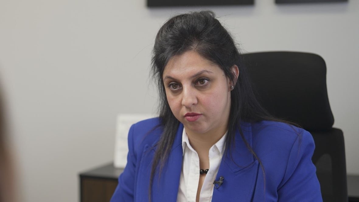 A woman in a blue suit sits at a desk.