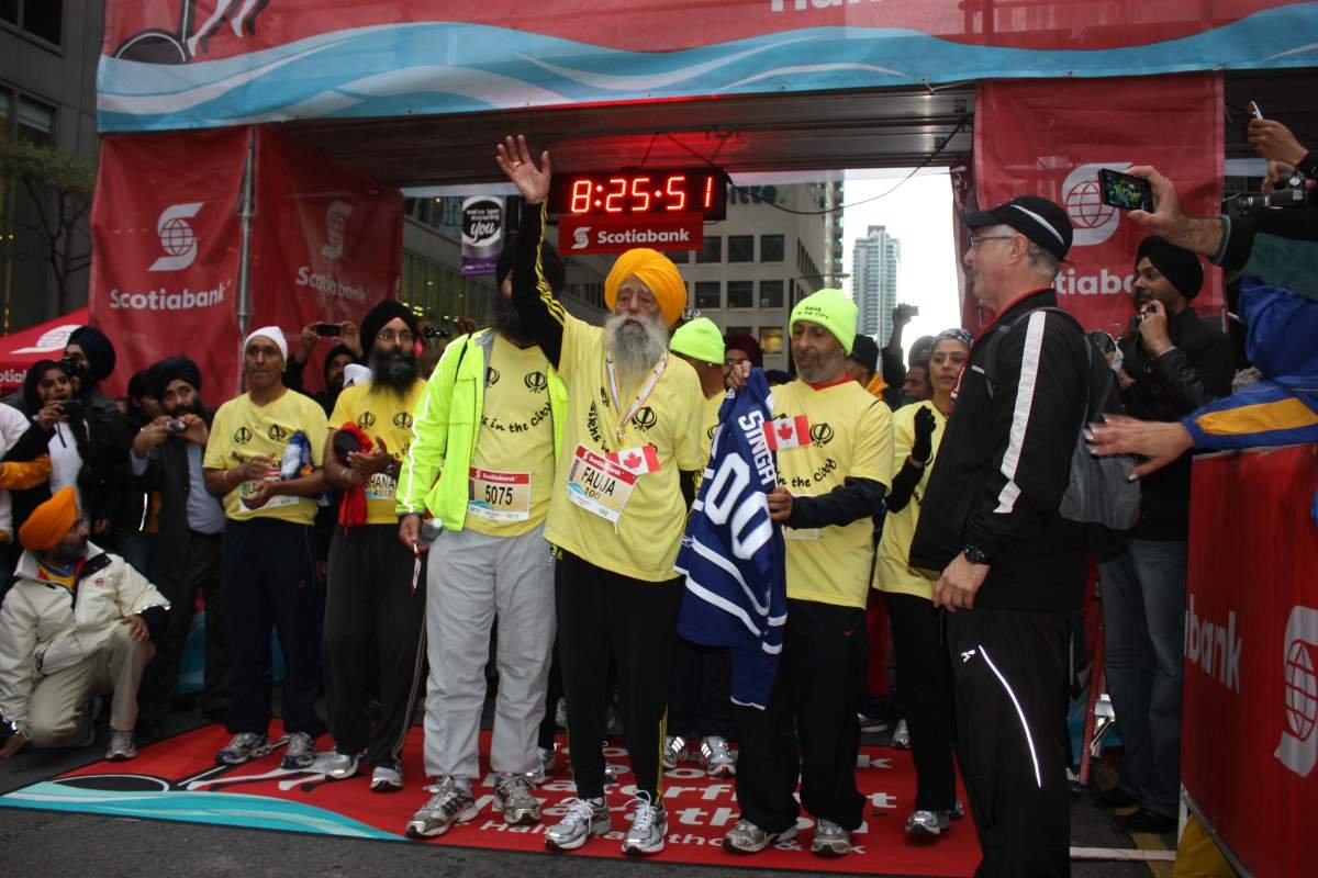Fauja Singh is shown crossing the finish line of the 2011 Toronto Waterfront Marathon, surrounded by his coach and supporters.