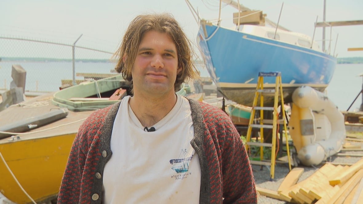 A man stands in front of a boat on the waterfront