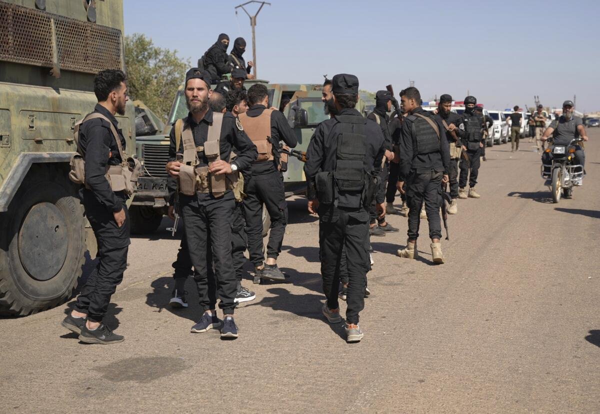 People stand or walk along military vehicles on a road.