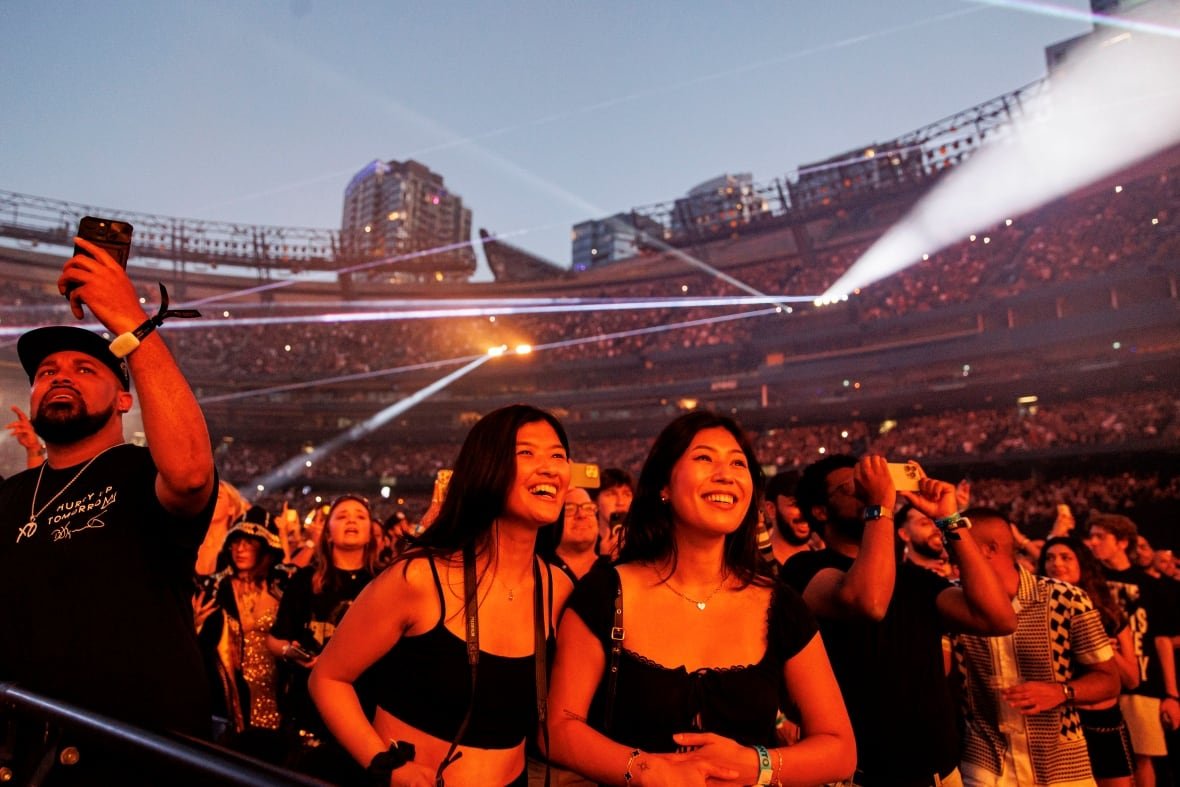 A smiling pair of women stand in front of a large crowd behind them.