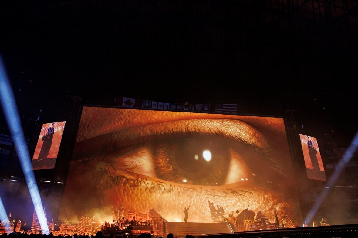 A large eye is seen projected on a screen on a stage.