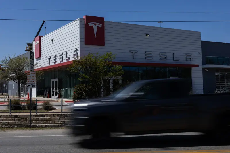 A truck drives in front of a large building with the Tesla logo.