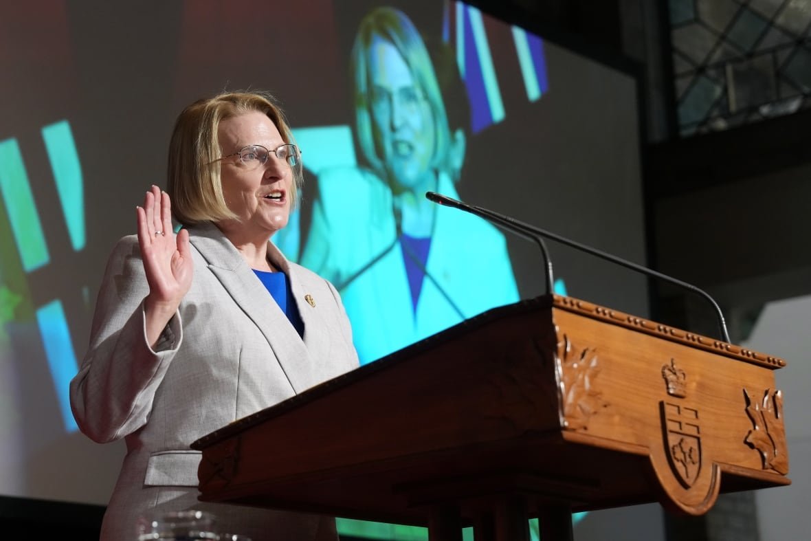 A woman in formal attire speaks behind a wooden lecturn.