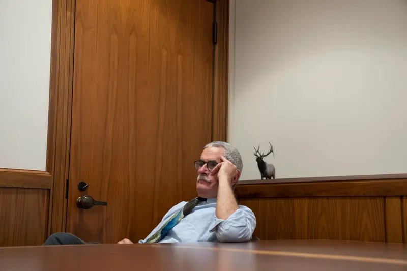 Golden sits in a wood-paneled room with his elbow on a table, leaning his head against his hand.