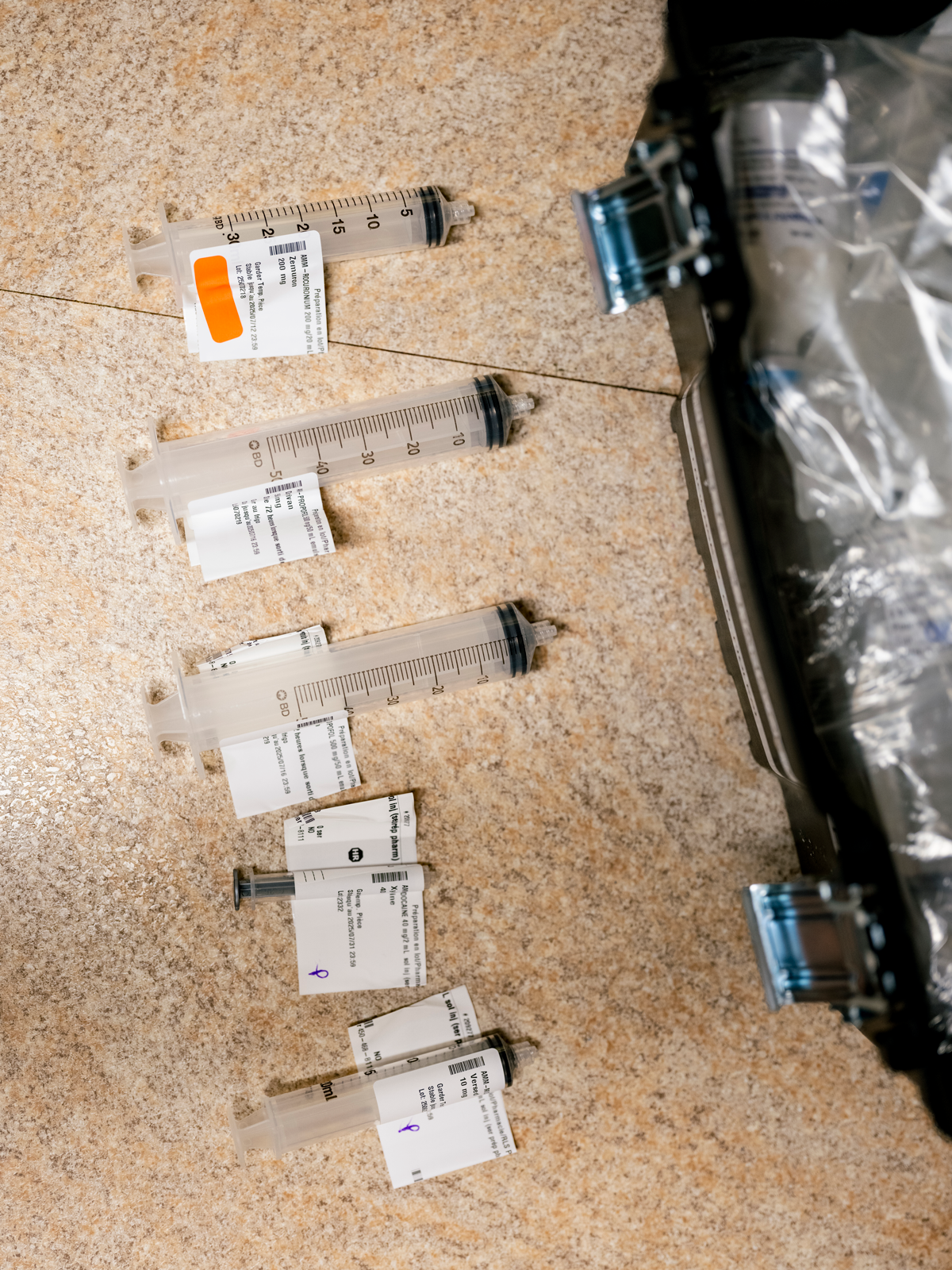 photo of a row of 5 various-sized labeled syringes lying on table next to case